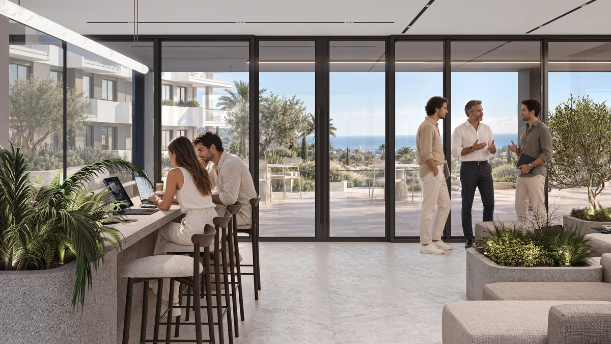 Residents working and socialising in the coworking lounge overlooking the landscaped courtyard and sea.